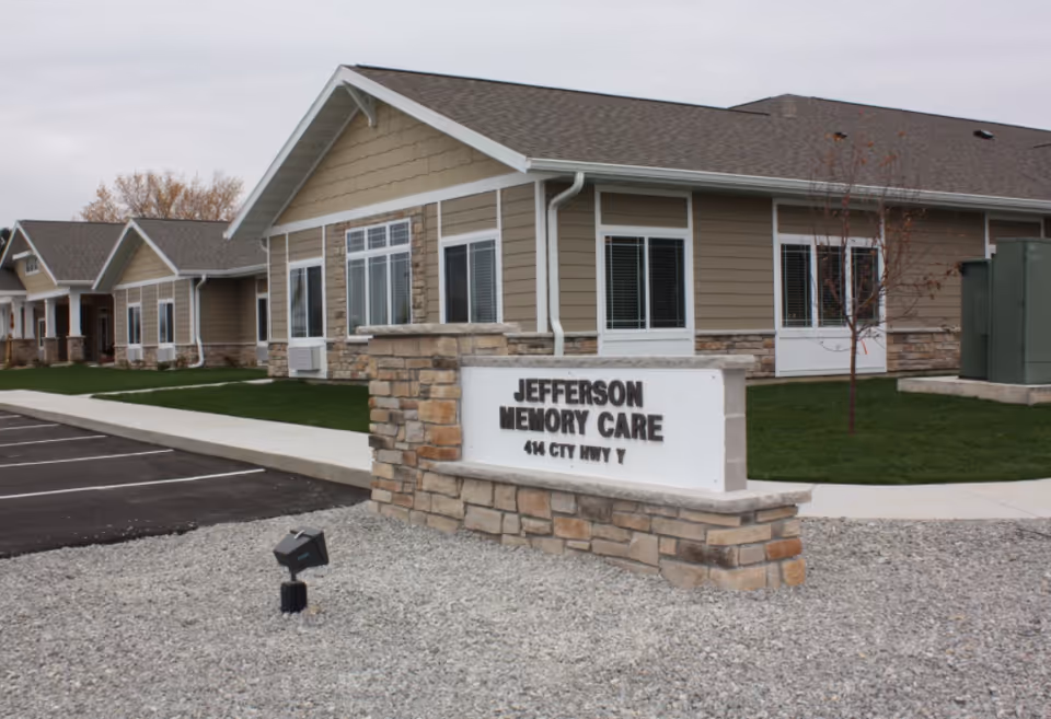 Front exterior of Jefferson Memory Care showing a stone sign and a single-story beige facility building.