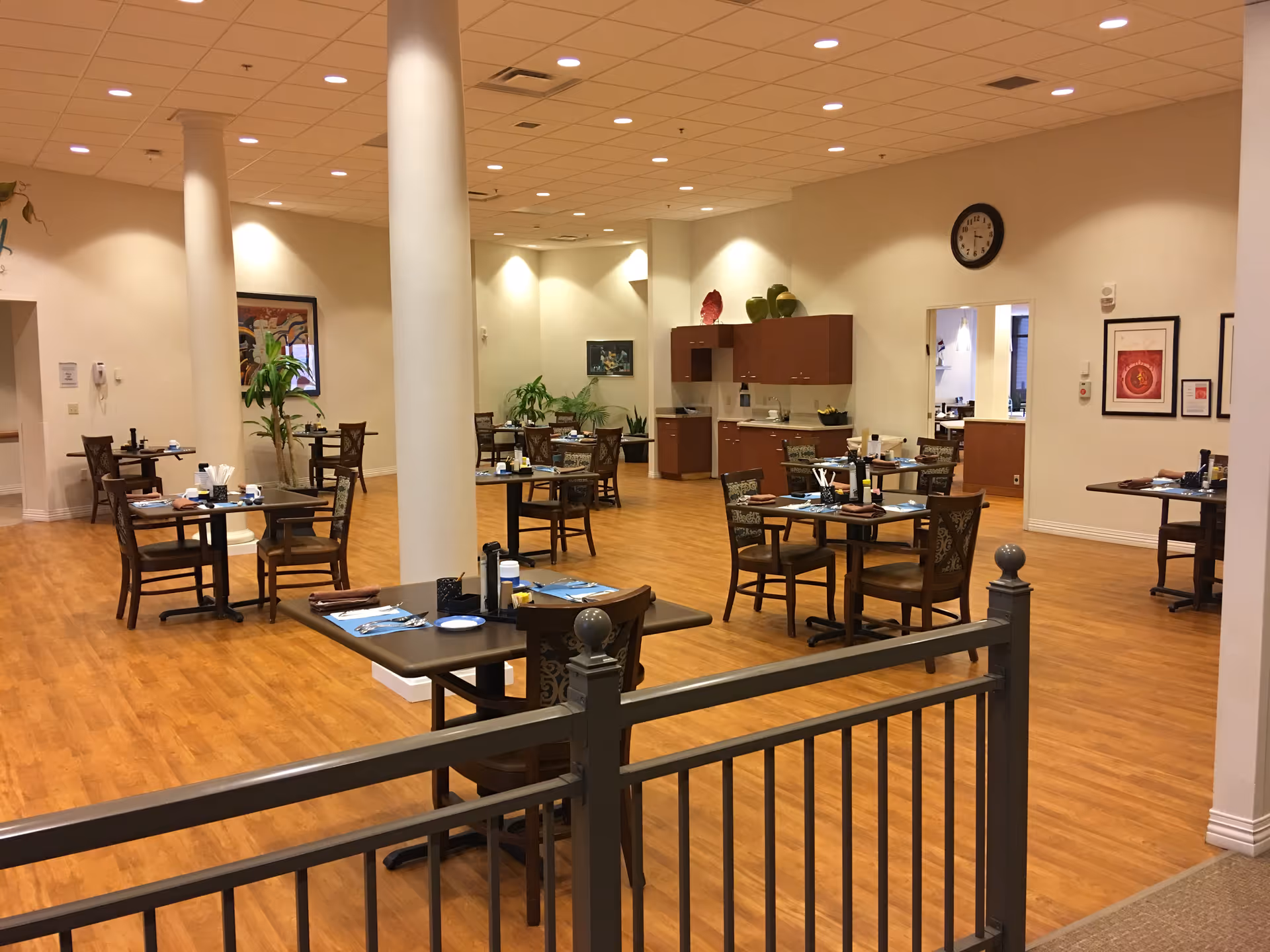 Spacious dining room with multiple set tables, wood floors, columns and a small serving area in the back.