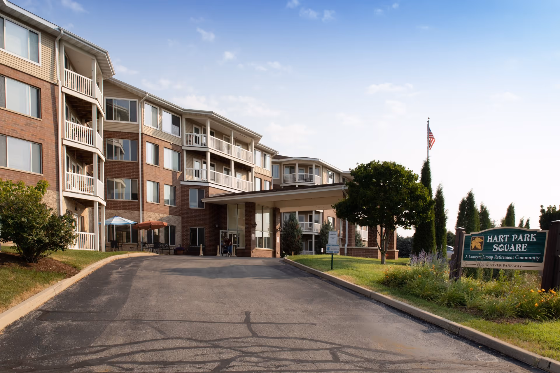 Front entrance of a multi-story brick senior living building with a drive-up canopy and a sign for Hart Park Square.