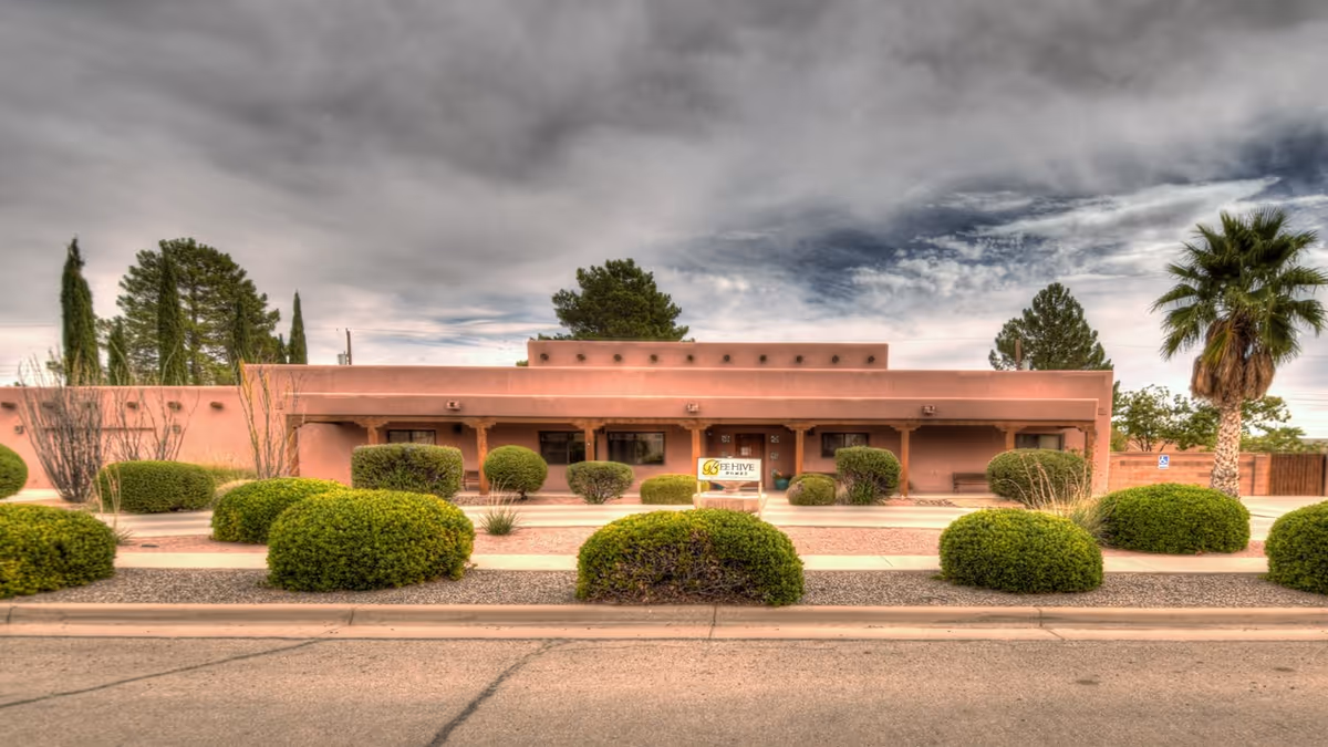 Pink adobe-style, single-story senior living facility with trimmed shrubs and a central sign.