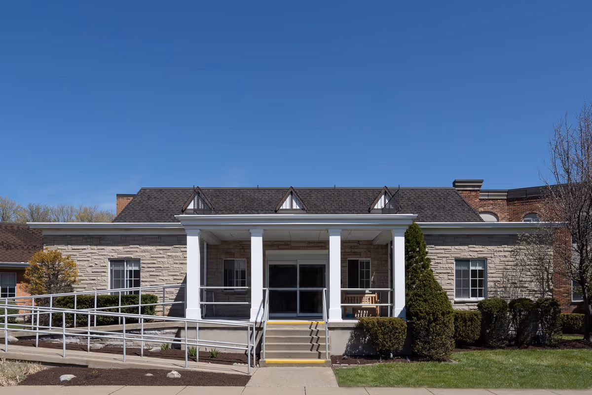 Front view of a single-story care center with a stone exterior, white columns, and a ramp leading to the entrance.