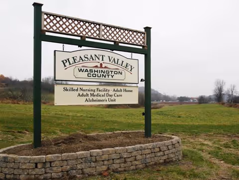 Outdoor sign reading Pleasant Valley, Washington County, on a green frame in a grassy area.