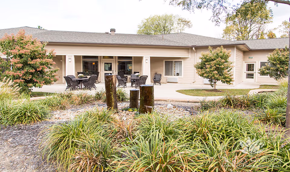 Front exterior of Ashley Gardens Assisted Living & Memory Care with a patio, outdoor seating, landscaped garden, and a small fountain.