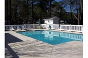 Outdoor swimming pool surrounded by a white fence with a small pool house and trees in the background.