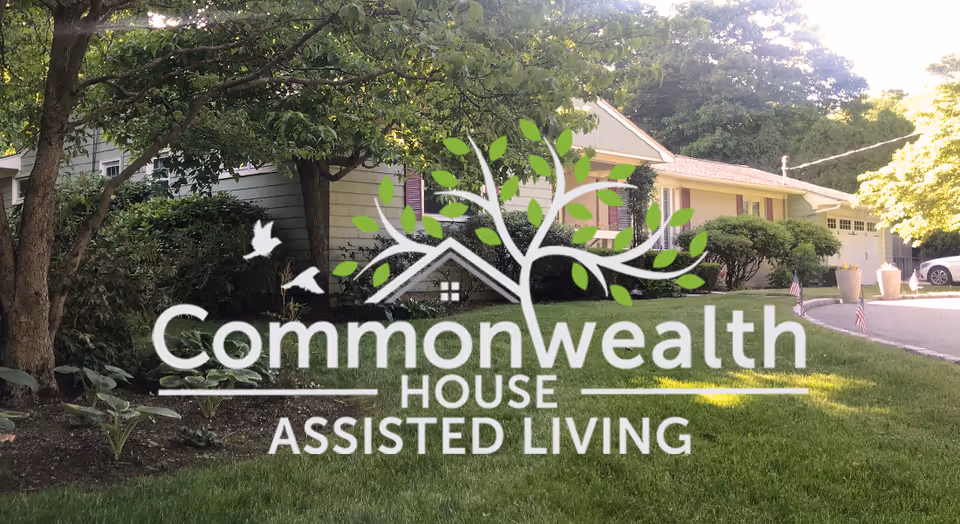 A single-story residential building with a well-maintained lawn, trees, and shrubs in front. The driveway is visible on the right side with a parked car. The image has a logo overlay in the center that reads 'Commonwealth House Assisted Living' with a graphic of a tree and birds.