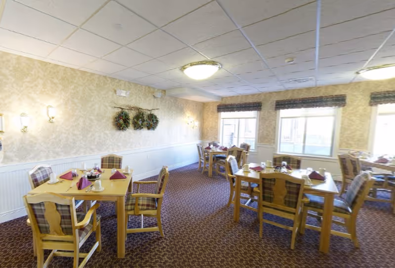 Bright dining room with wooden tables and upholstered chairs arranged with place settings and folded napkins.