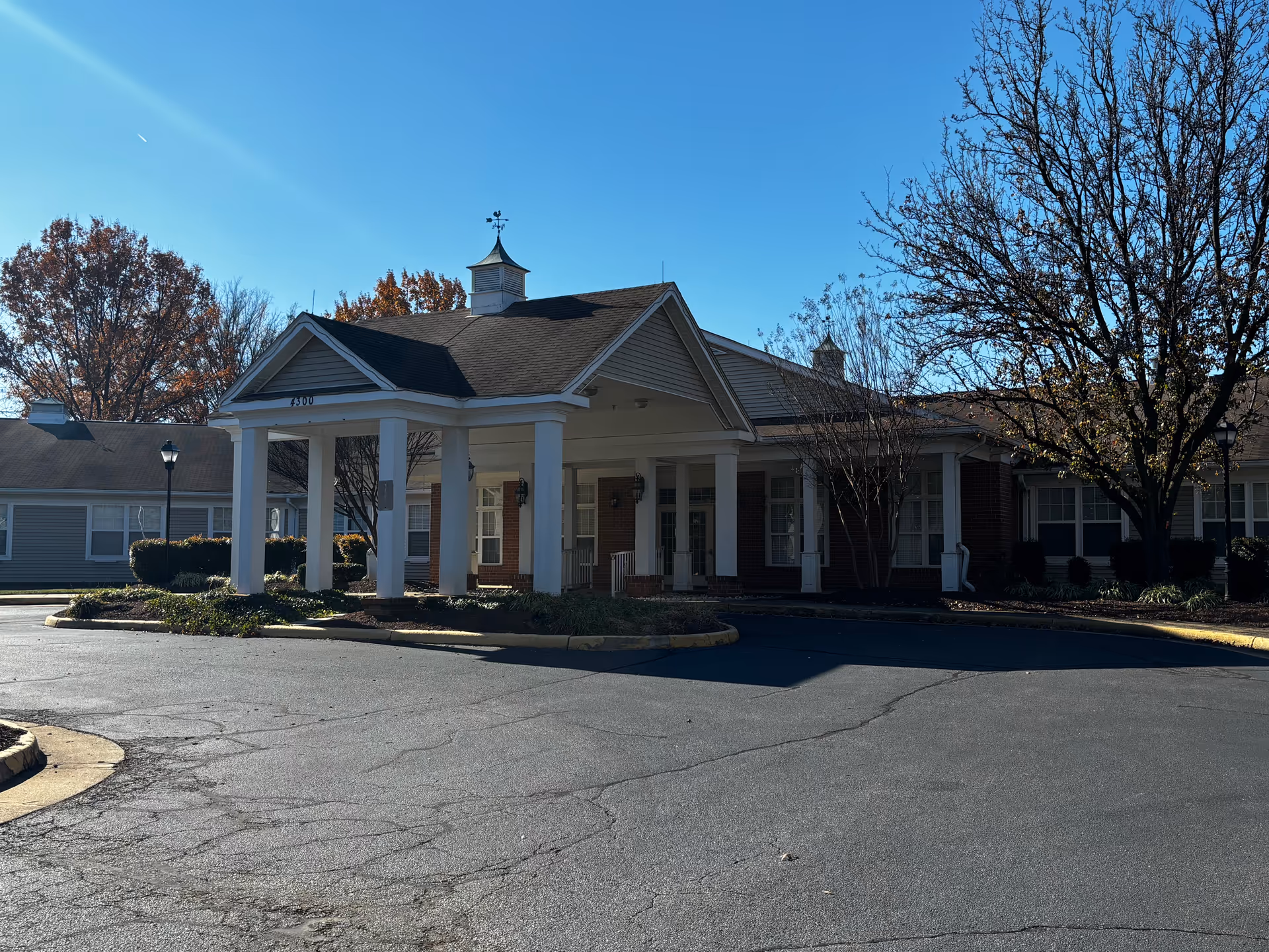 Front entrance of Sunrise of Fairfax with a covered portico, columns and circular driveway under a clear blue sky.