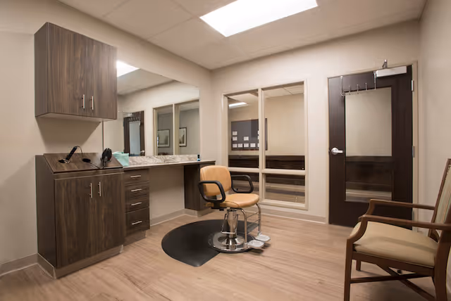 Small salon-style room with a barber chair in front of a large mirror, wood cabinets, and additional seating.