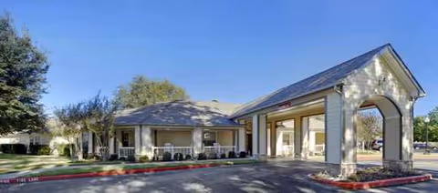 Single-story senior living entrance with a covered porte-cochere and landscaped parking area.