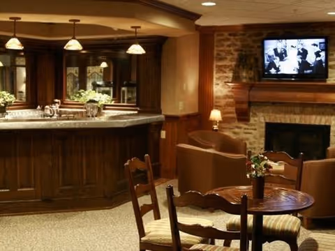 Cozy communal lounge with a wooden bar, round tables and chairs, armchairs, a stone fireplace and a wall-mounted TV.