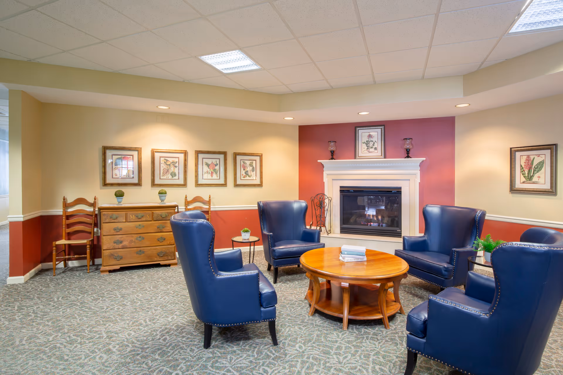 Cozy seating area with blue armchairs arranged around a wooden coffee table in front of a fireplace in a lounge.