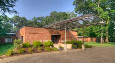 Brick nursing facility exterior with curved canopy over entrance and landscaped shrubs.
