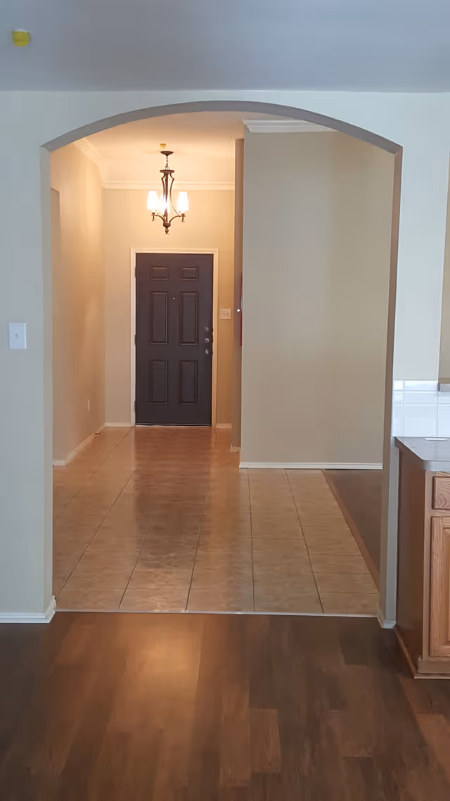 Archway opens to a tiled hallway with front door and hanging chandelier.