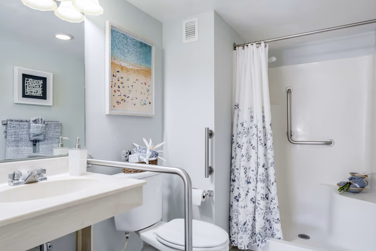 Accessible bathroom with sink, toilet, grab bars, and a shower with a floral curtain.