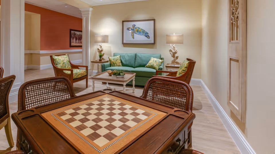 Community lounge with a chessboard table in the foreground, a green sofa, armchairs and lamps.