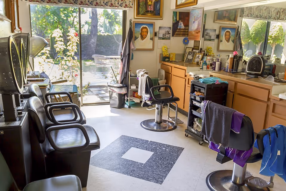 Well-lit salon/hair-styling room with barber chairs, mirrors, hair dryers and cabinets opening to an outdoor patio.