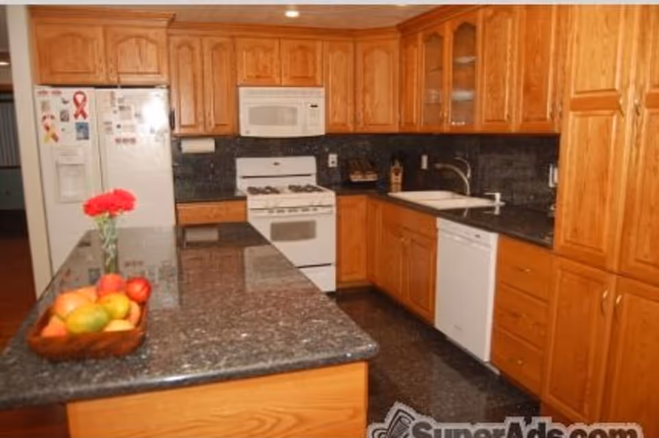Kitchen with wooden cabinets, granite countertops and island topped with a fruit bowl and flowers.