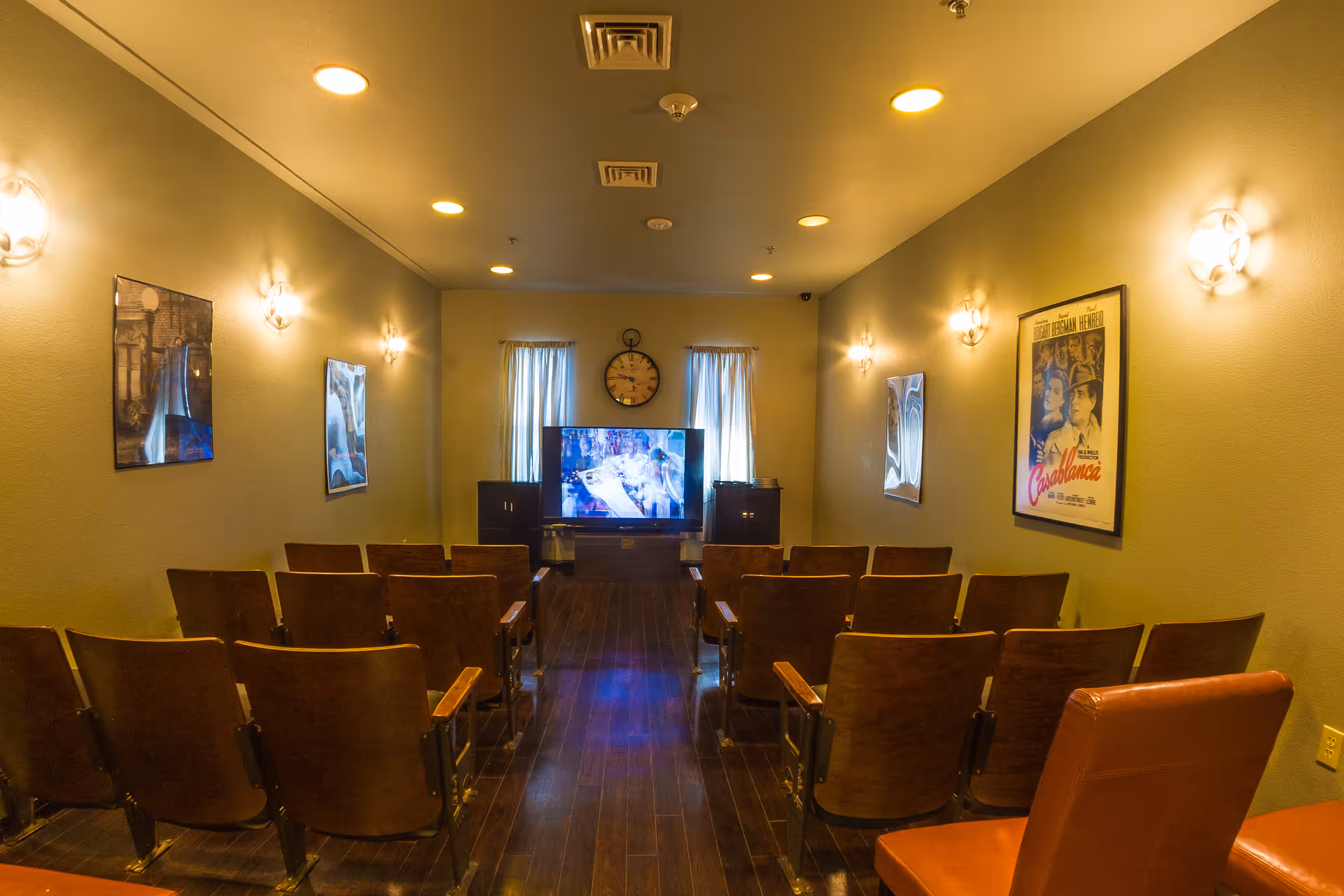 Small screening room with rows of wooden theater seats facing a TV and vintage movie posters on the walls.