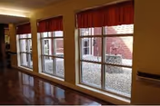 Interior hallway with large windows and red valances overlooking a courtyard, shiny wooden floors and a wall handrail.