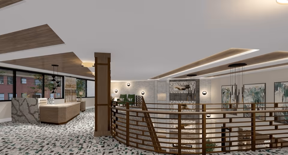 Spacious modern interior lobby with a curved wooden railing overlooking a lower level, a reception desk, seating areas, and contemporary lighting and artwork.