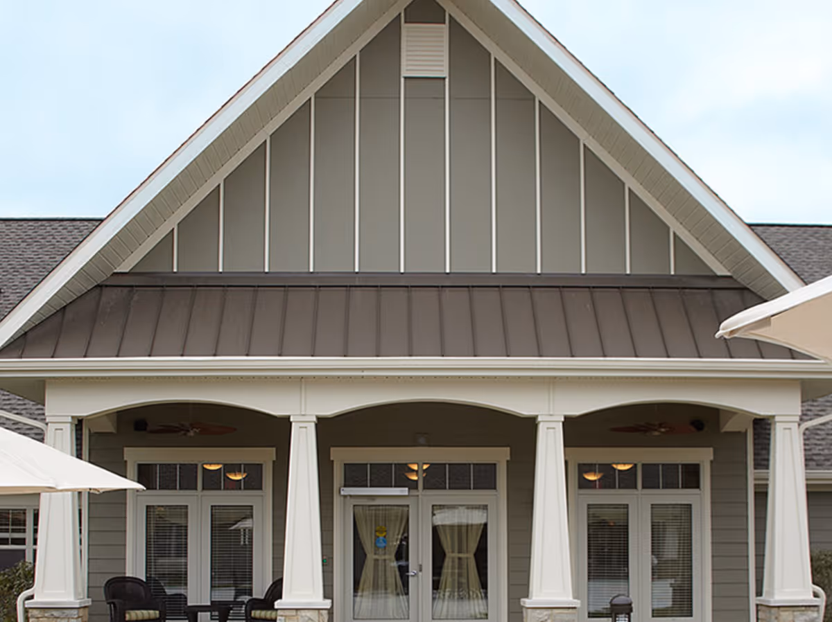 Front porch entrance of a residential-style building with columns, double glass doors, and a gabled roof.