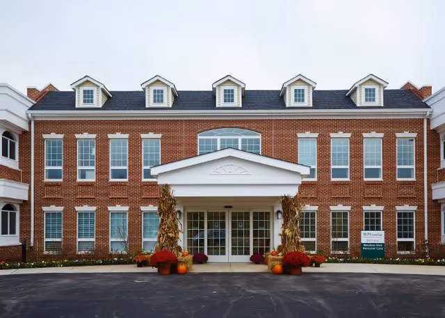 Red brick senior living building with white entrance portico and fall decorations.