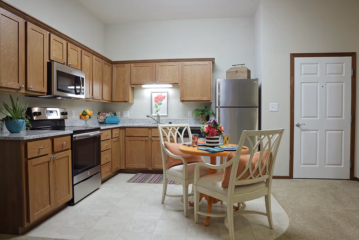 Open kitchen with wooden cabinets, stainless steel appliances and a small round dining table with four chairs.