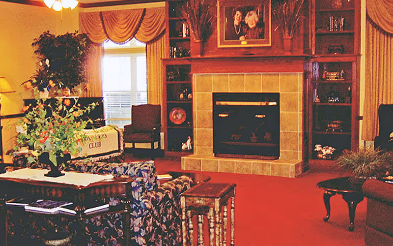 Cozy living room with a central tiled fireplace flanked by built-in shelves, upholstered seating, side tables, and decorative plants.