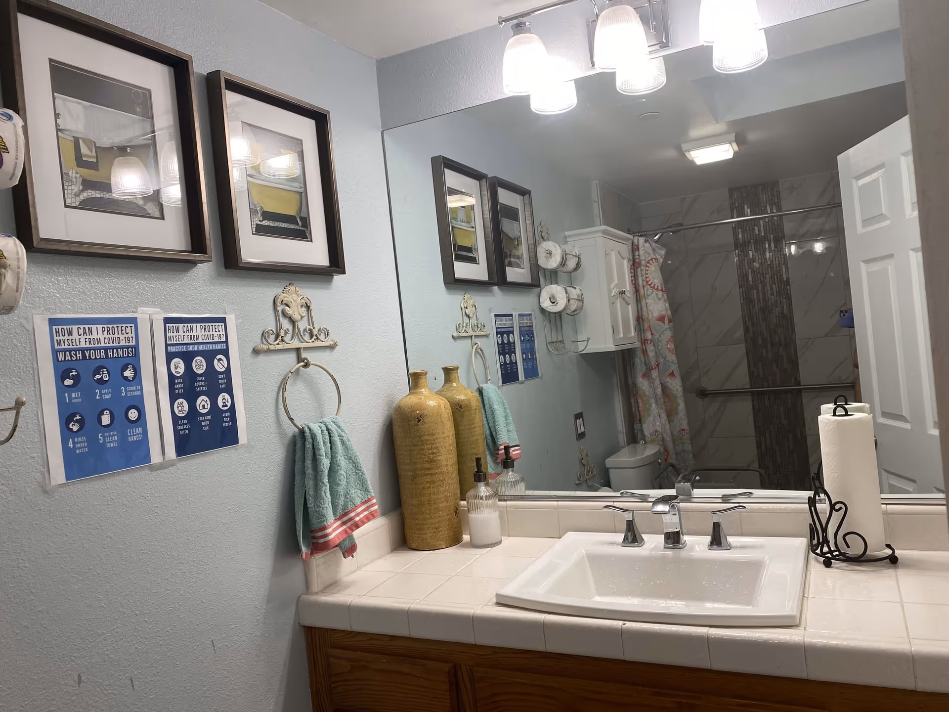 Bathroom vanity with sink, mirror, decorative vases, towel ring, and a shower with curtain visible in the mirror reflection.