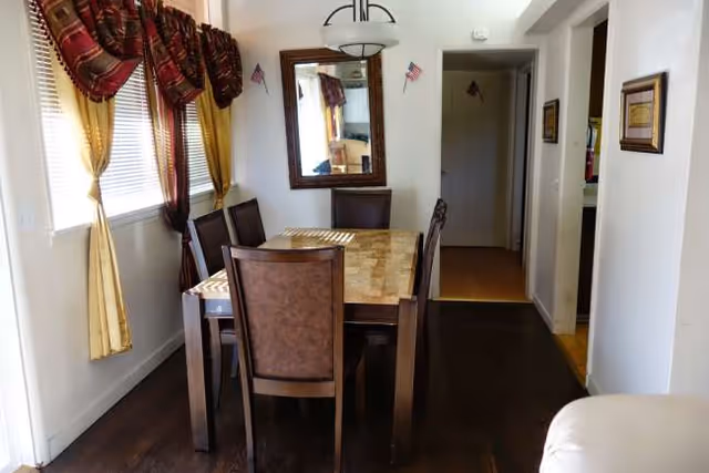 Dining room with a wooden table, several chairs, mirror, and windows with curtains.