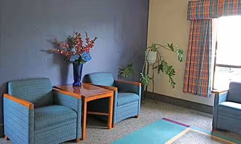 Two blue upholstered chairs with a wooden table and flowers in a cozy lounge.