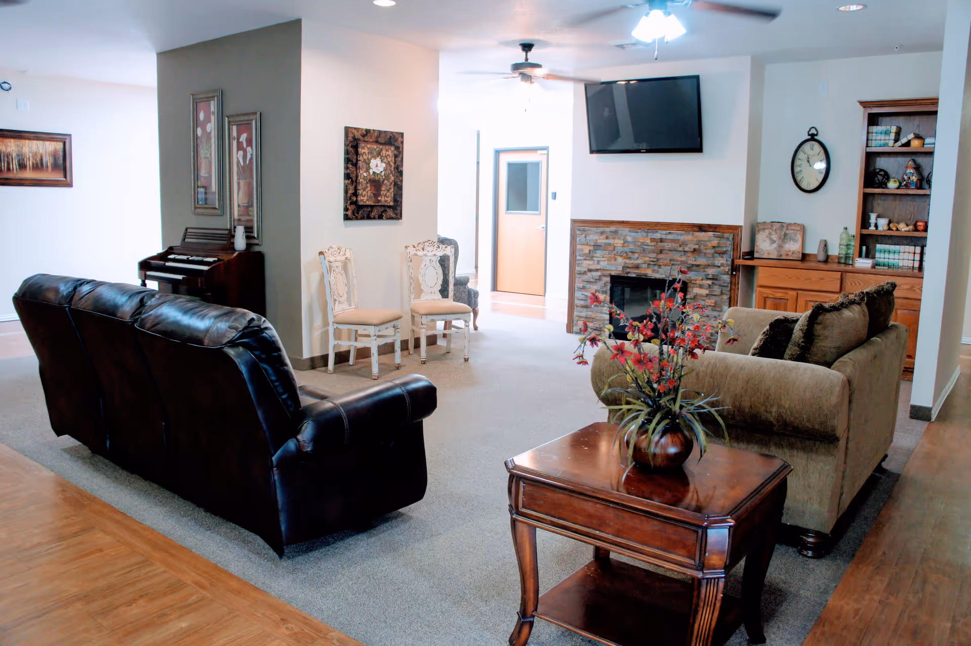 Shared living room with leather and fabric sofas, a wooden coffee table with a floral arrangement, wall-mounted TV and fireplace.