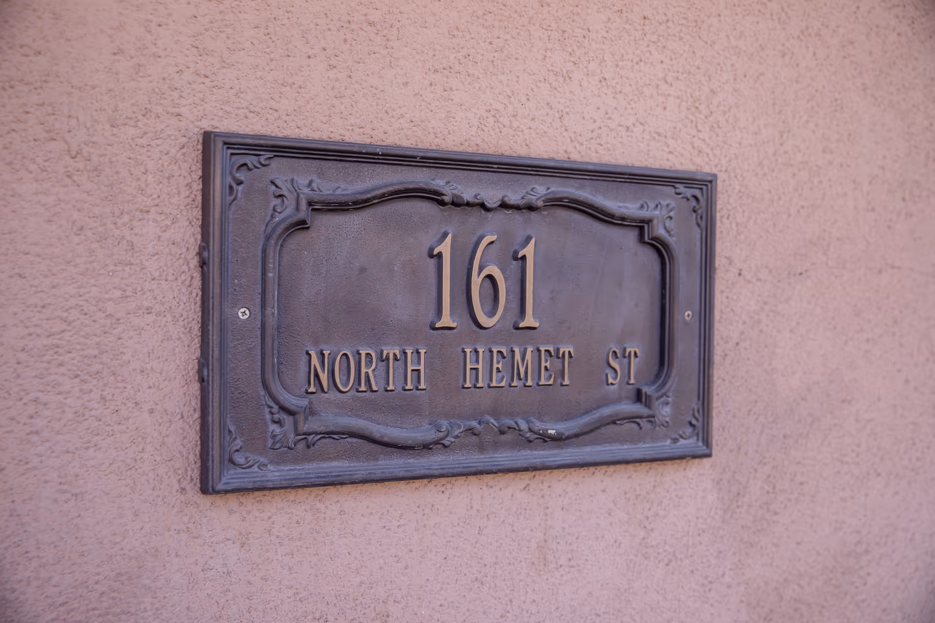 A decorative metal address plaque mounted on a textured wall displaying the number 161 and the street name North Hemet St.