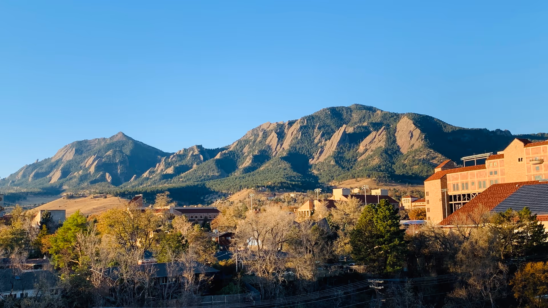 View of a mountain range with buildings and trees in the foreground under a clear blue sky.