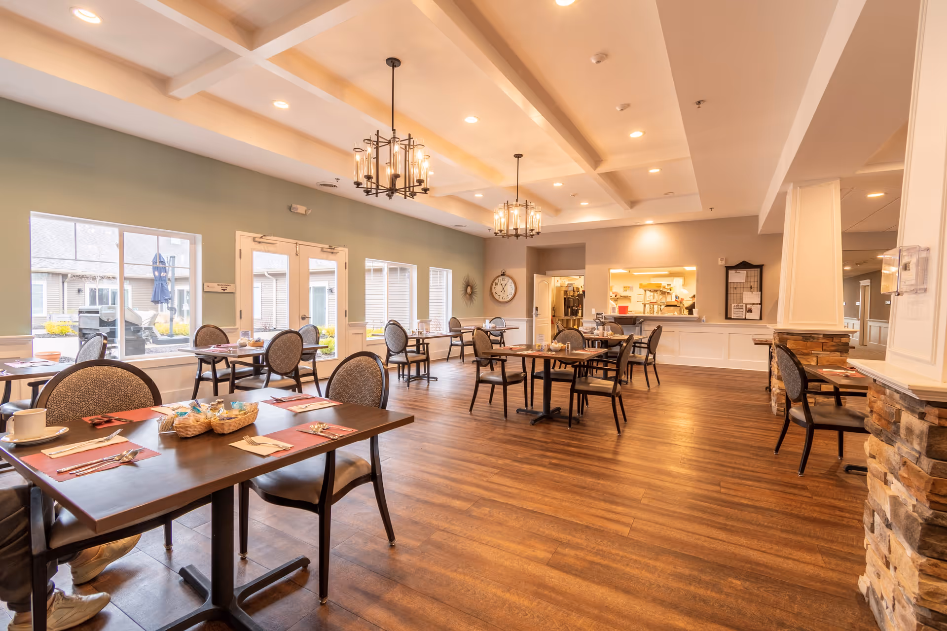 Spacious dining room with wooden floors, multiple set tables and chandeliers, and large windows overlooking a courtyard.