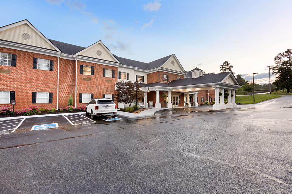 Front exterior of a two-story brick senior living building with a covered entrance and a parked white SUV.