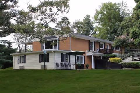 Two-story brick-and-siding senior living facility exterior with a grassy lawn and seating.