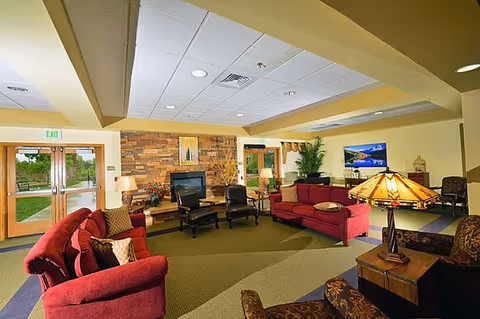 Community lounge with red sofas and armchairs arranged around a stone fireplace, a television, and decorative lamps.