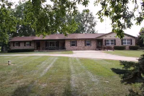 Single-story brick senior living facility with a manicured lawn and trees in front.