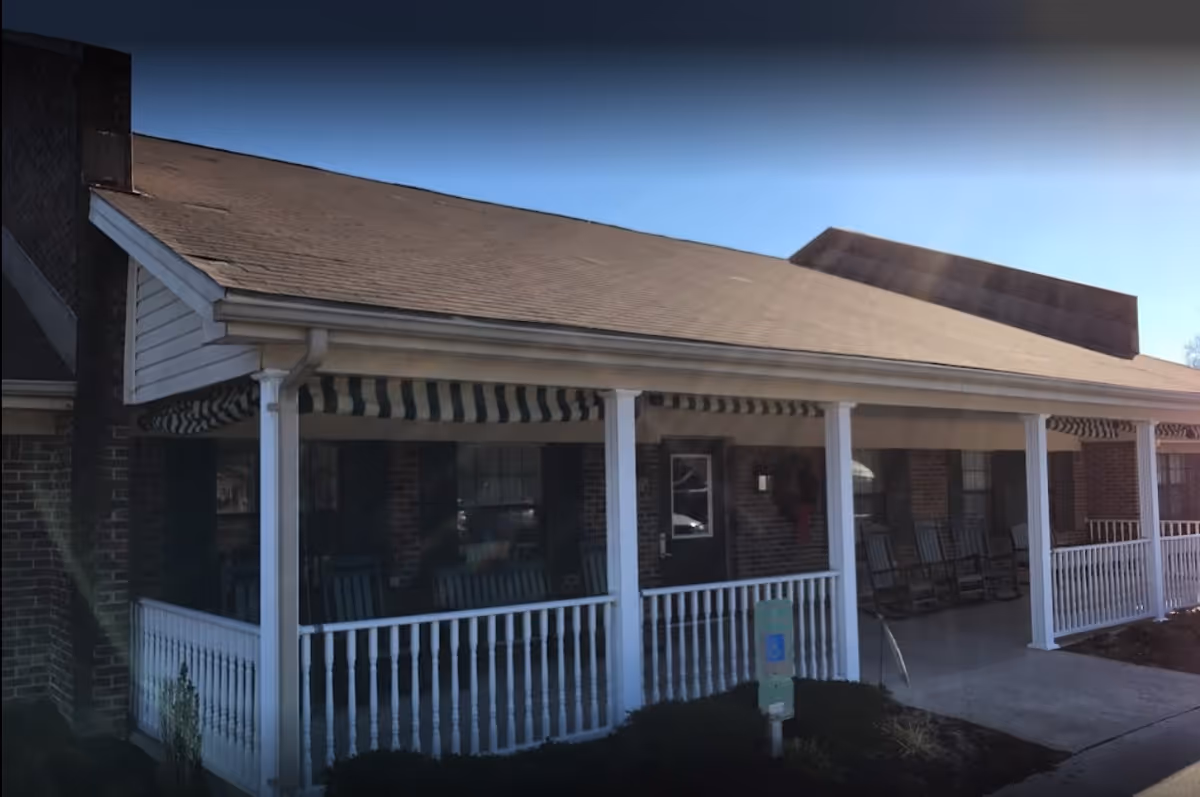 Brick building's covered front porch with white columns, railing, striped awning and rocking chairs at the entrance.