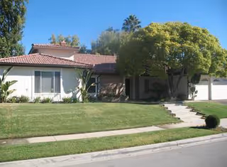Front exterior of a single-story senior care home with a manicured lawn and trees.