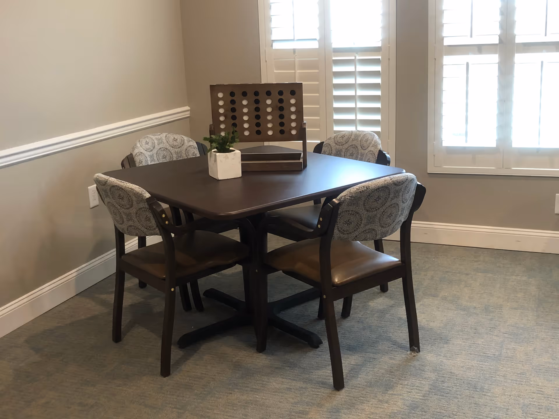 Dining table with four upholstered chairs in a sunlit senior living dining room