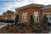Brick and stone front entrance of a retirement center with landscaped flower beds and two arched decorative window panels.