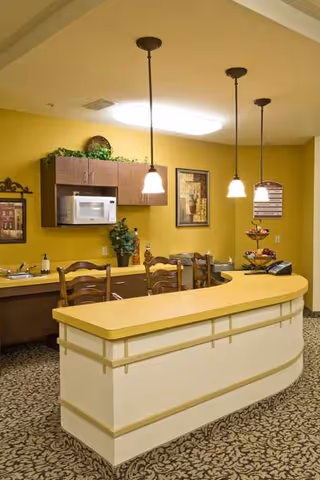 Yellow-walled dining area with curved beige counter, pendant lights, microwave, and wooden chairs.