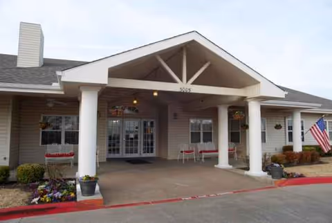 Front entrance of Lakewell Court senior living facility with columns, seating, and flowers.