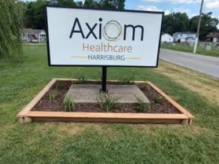 Outdoor freestanding sign that reads "Axiom Healthcare Harrisburg" set in a landscaped bed beside a road.