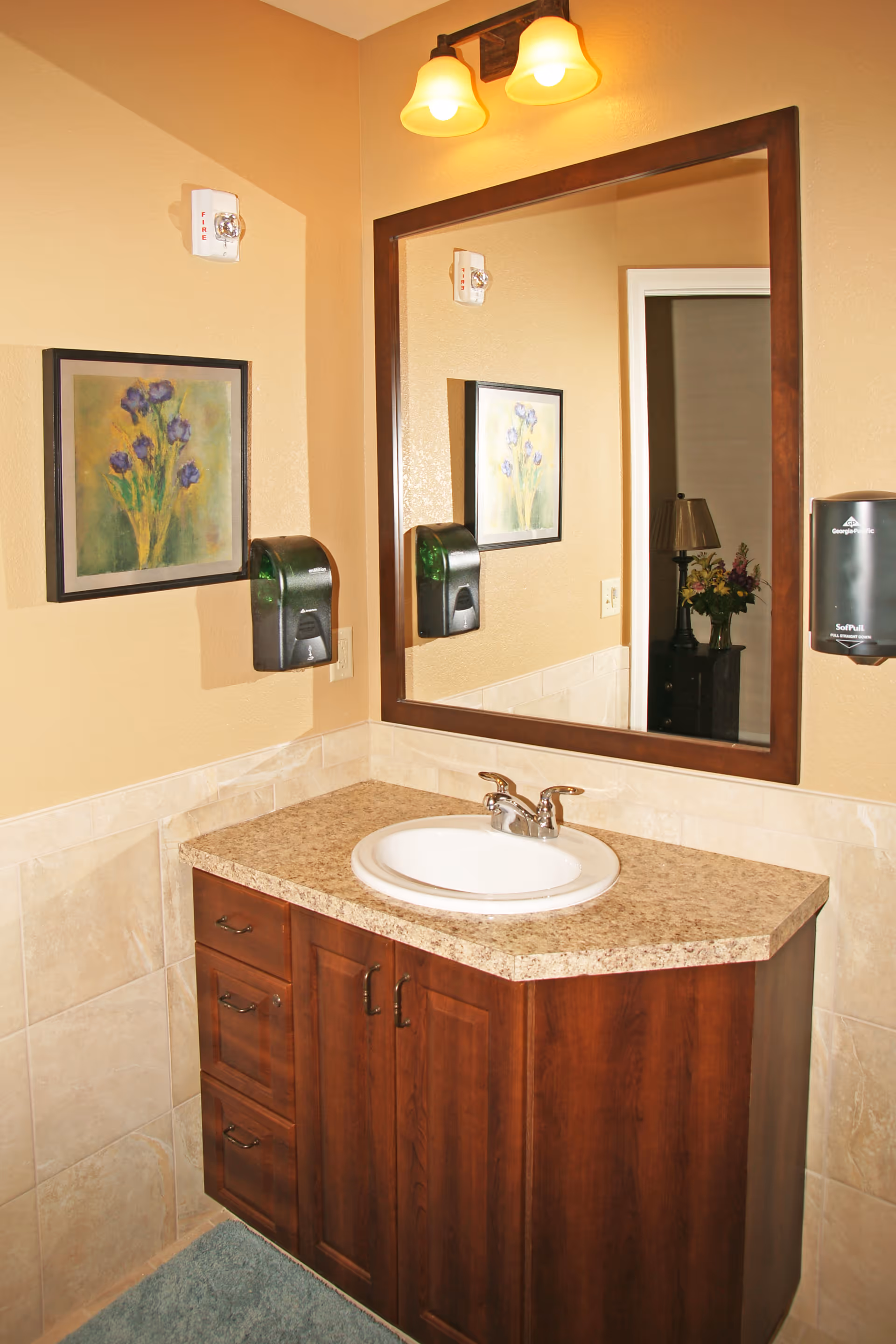Bathroom vanity with a sink, large mirror, wall-mounted soap dispensers and framed artwork.