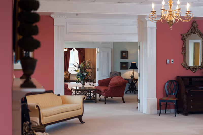 An elegant interior lounge with upholstered sofas and armchairs, a coffee table with flowers, decorative columns and a chandelier.