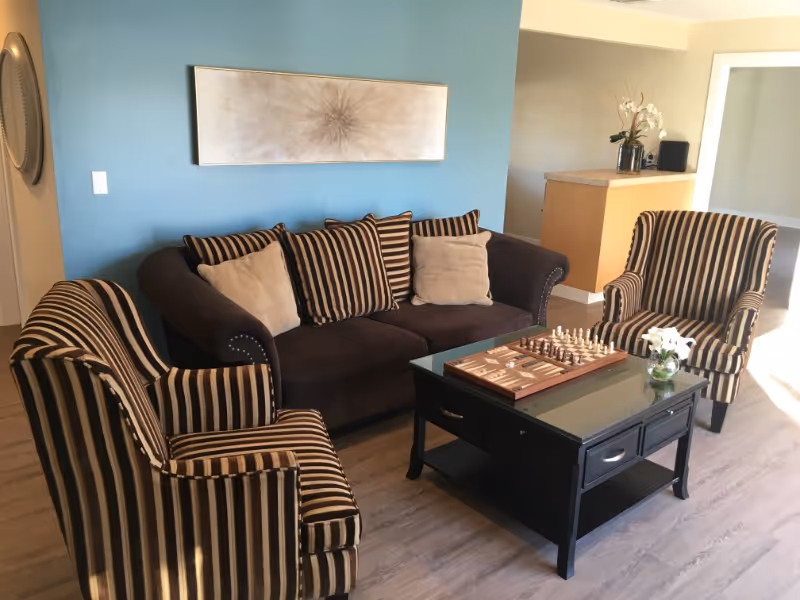 Cozy living room with a brown sofa, two striped armchairs, a black coffee table with a chess set, and a teal accent wall.