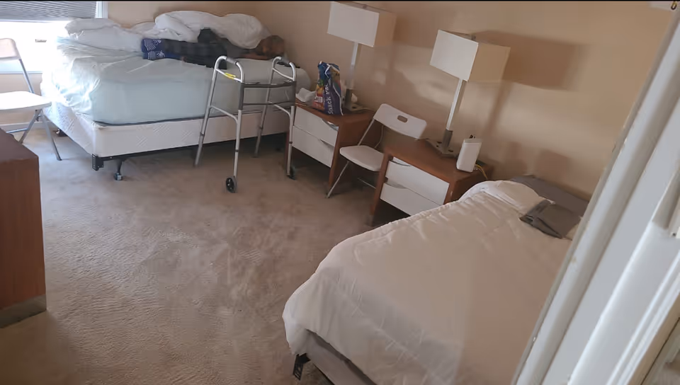 Two beds and nightstands in a shared senior living bedroom with lamps.